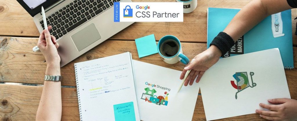 Flatlay eines Tisches mit Laptop, Unterlagen und Kaffeetasse. Zwei Kolleginnen sprechen über die Vorteile eines Google CSS-Partners.